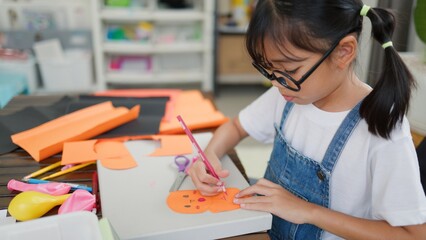 Asian girl focused on making a DIY craft project at home using a compass and colorful paper, promoting creativity, fine motor skills, and fun learning in a homeschool setting.