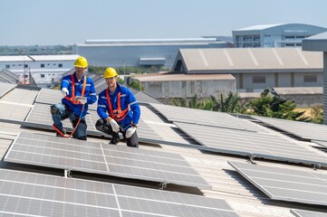 Two solar panel technicians in hardhats and safety gear install solar panels on a commercial...