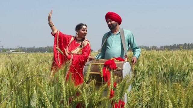 Punjabi sikh couple celebrating Baisakhi or vaisakhi festival in agriculture field and doing bhangra dance and play dhol. Culture of india. People of punjab.