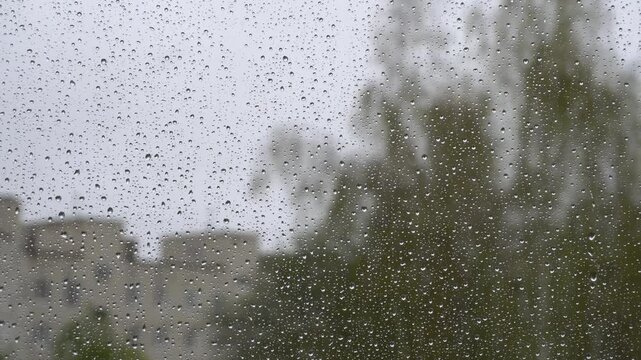 Rain drops falling on window glass blurring city view