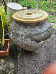Large, rustic water jar with a light-colored lid.