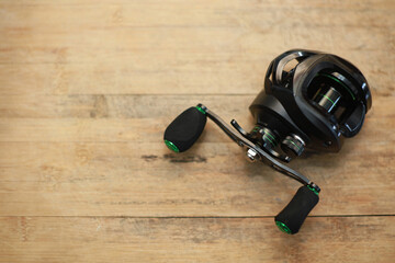 Black water drop fishing reel on wooden floor with copy space