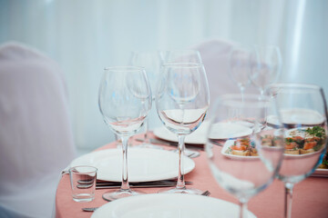 Preparation for the event at the restaurant. Wine glasses, glasses, plates, forks, knives on a light background and a pink tablecloth. Beautiful blurred background with copy space