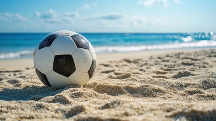 Classic black and white soccer ball resting on sandy beach with blue ocean and horizon in background