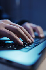 A man in a dark hoodie uses a laptop at night, symbolizing cybercrime, hacking, identity theft, and...