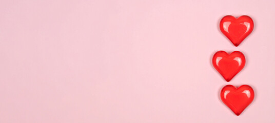 three red hearts made of semi-transparent plastic on a pastel-colored background with copy space on the left