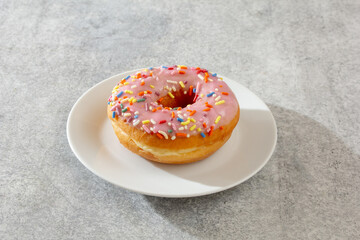 A view of a pink frosting rainbow sprinkles donut.