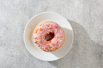 A top down view of a pink frosting rainbow sprinkles donut.