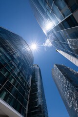Low-angle view of modern glass skyscrapers against a clear blue sky. Sunlight highlights the reflective surfaces