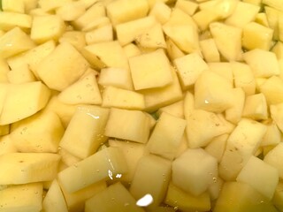 Close up potato slices soaked in water in a container, prepare for cooking. Seasoning before cooking