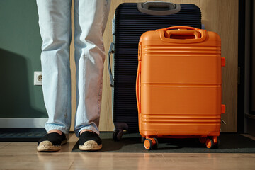 Close up of woman wearing jeans and shoes standing near suitcase ready to leaving home for travel....