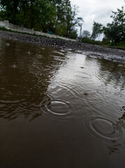 Puddle of water with drops of rain in cloudy weather