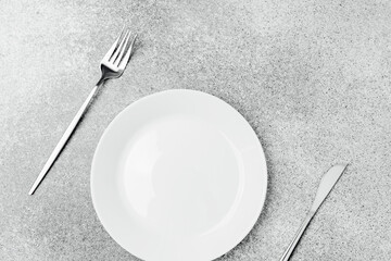 Empty plate and cutlery arranged for a meal on a gray table surface