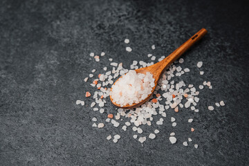 Wooden spoon filled with pink himalayan salt on textured black surface