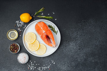 Fresh salmon steak with lemon and herbs on a dark stone table