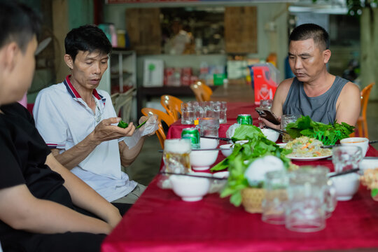 Group of diners enjoying traditional Asian cuisine in a casual setting while engaged in conversation and mobile activities
