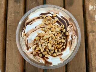 Close up a cup of vanilla ice cream with caramel syrup and peanut crumbs on the top. Sweet. cold, and delicious ice cream