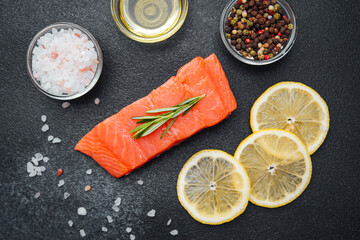 Fresh salmon fillet with herbs, lemon slices, and seasonings on dark stone