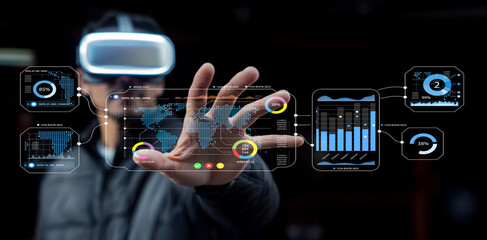 Young man using virtual reality headset interacting with futuristic digital interface displaying charts and graphs in dark background