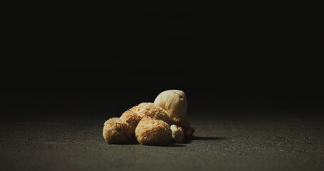 Dark, shadow and teddy bear in studio for neglect, isolation and forgotten toy on ground. Night,...