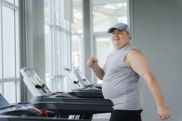 Fat man running on a treadmill in a gym