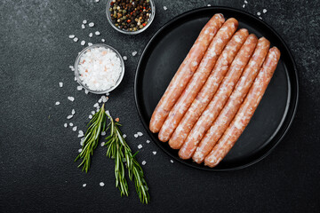 Raw pork sausages on black plate with rosemary and pepper