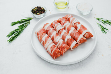Bacon wrapped sausage rolls on white plate with herbs and oil