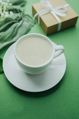 Coffee cup, gift and lily of the valley bouquet on green table background..