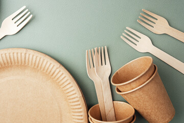 Disposable eco paper cups and wooden forks on green background flat lay view