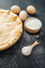 Preparing pie dough with a rolling pin and different baking ingredients set out.