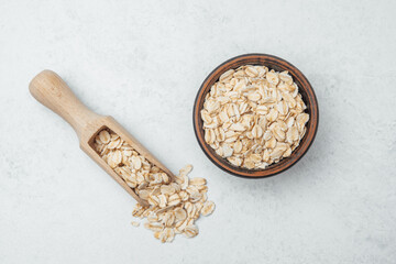 Oats in a wooden bowl with a scoop placed beside it on a light background