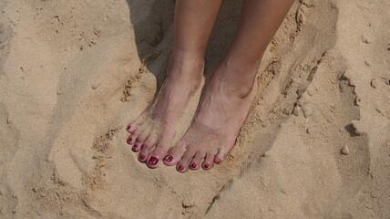 Female feet with red toe nail color on a sandy beach