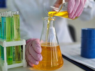 Scientist in lab pouring yellow liquid from flask into beaker while wearing gloves during experiment concept