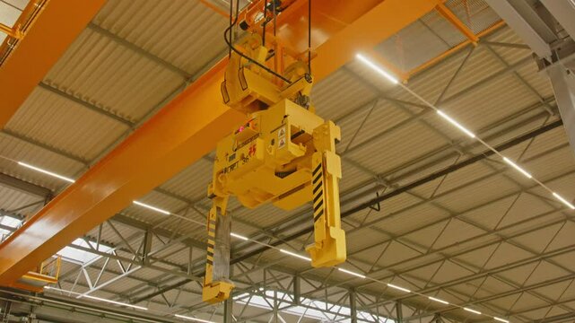 A large clamp crane in a big factory goed down and grabs a heavy steel coil