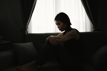 A young woman sits alone indoors in dim light, overwhelmed by sadness, anxiety, and emotional...