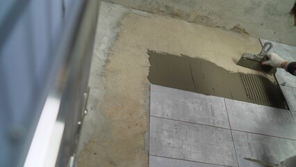 Construction worker applying cement glue to wall with notched trowel