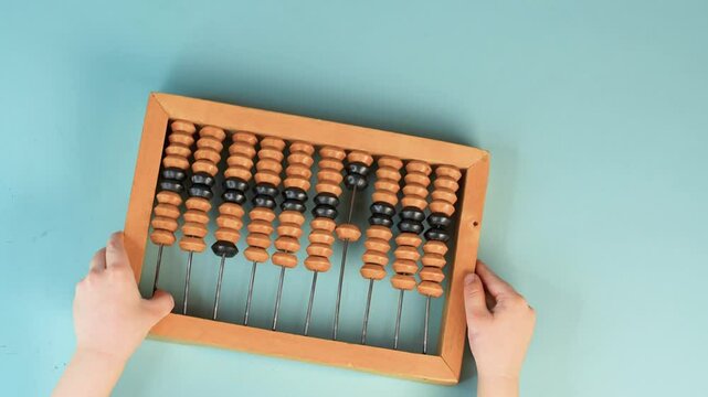 Little child's hands hold wooden abacus on a blue background. Close up, point of view shot. View from above.