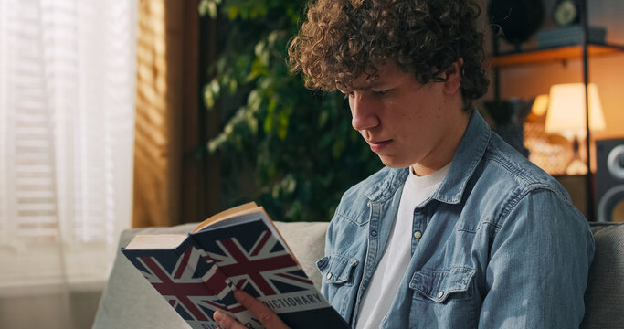 A teenager concentrates on a language task, sitting in a student room with an English book in front of him.