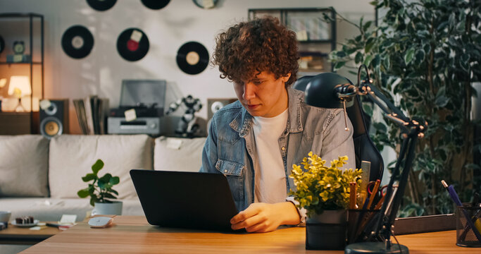 A young man sits a leather chair in front of a laptop, struggling to log into his online account while thinking about possible solutions.