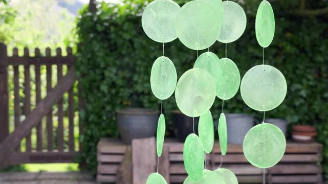 An acoustics wind chime mobile with green capiz shells hanging in a sunny garden and moving in the wind
