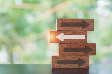 white arrow  on wooden block heading difference way from group with blurred nature background...