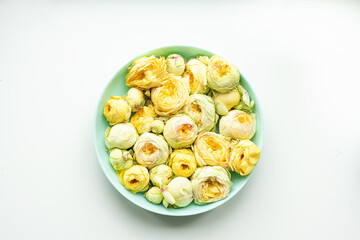 Yellow peony roses and buds in a soft blue plate on a white background. Fresh and natural floral composition. Ideal for spring or wellness concepts.