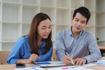 Two asian business people discussing and analyzing charts and data at office meeting