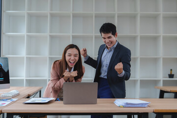 Excited business team celebrating success while working on laptop in office