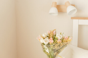 Bouquet of pink and white tulips with mimosa in a glass vase in a bedroom. Spring flower arrangement for interior decoration.