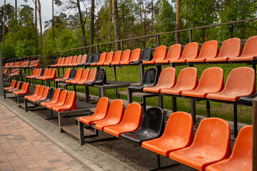 Rows of empty orange and black plastic seats on the grandstand near the outdoor sports stadium