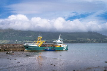Fishing boats anchor in a serene harbor, surrounded by green mountains and fluffy clouds, creating a tranquil atmosphere for marine and nature explorations, Carlingford, Ireland