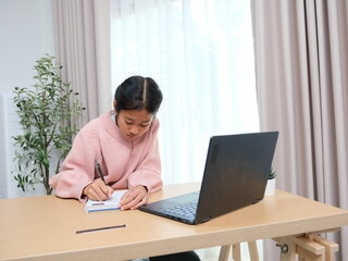 A girl is sitting at a desk with a laptop and a notebook