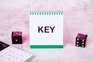 The word key on a notepad on the table next to a calculator and playing dice