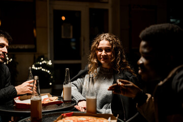 Friends enjoy casual evening with pizza and drinks at outdoor table in urban setting